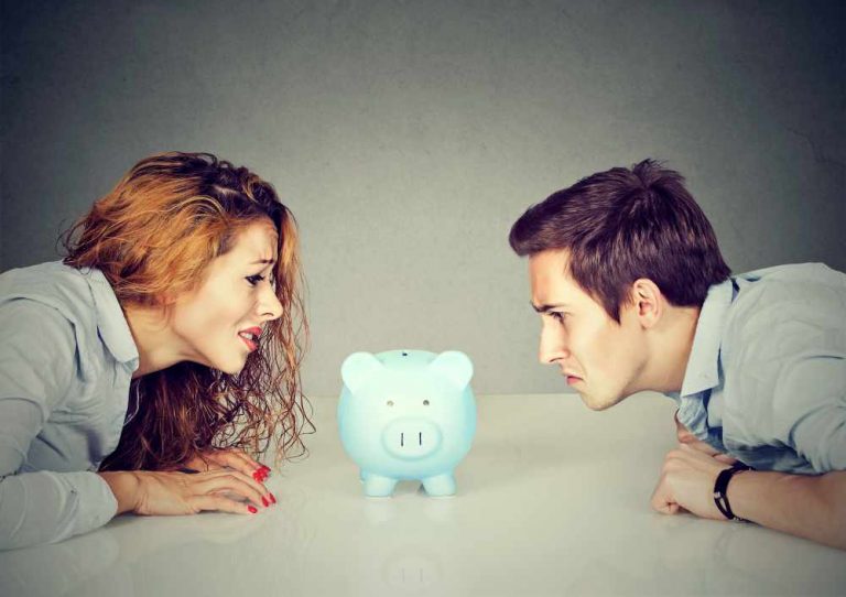Finances in divorce concept. Wife and husband can not make settlement holding piggy bank sitting at table looking at each other with hatred