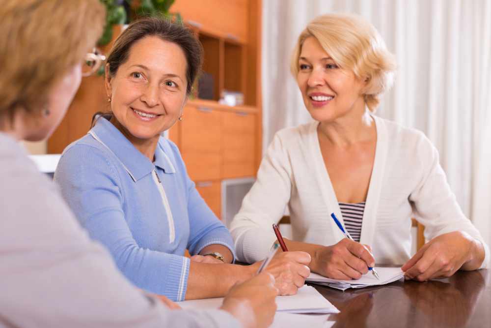 Positive senior ladies signing documents at notary. Focus on brunette