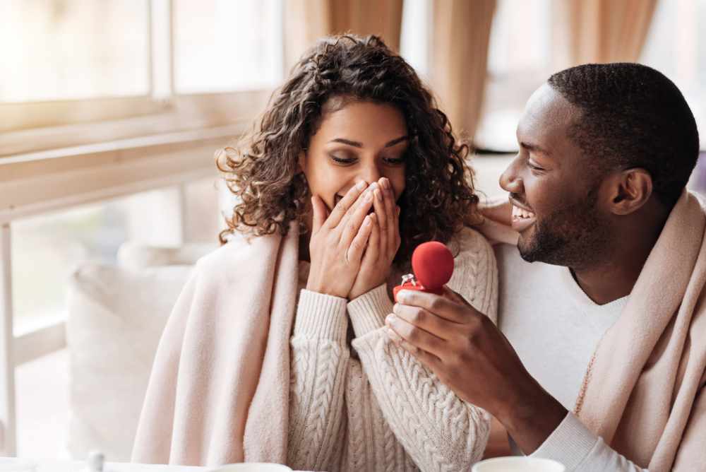 I love you. Amazed surprised positive African American couple sitting in the cafe and being covered with a blanket while getting engaged