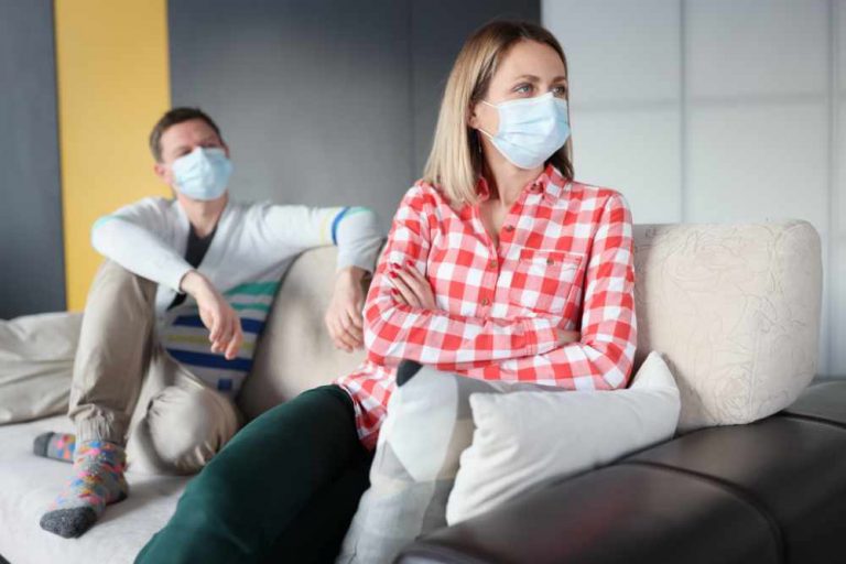 Offended woman and man are sitting on couch wearing protective masks. Increase in divorces after quarantine concept
