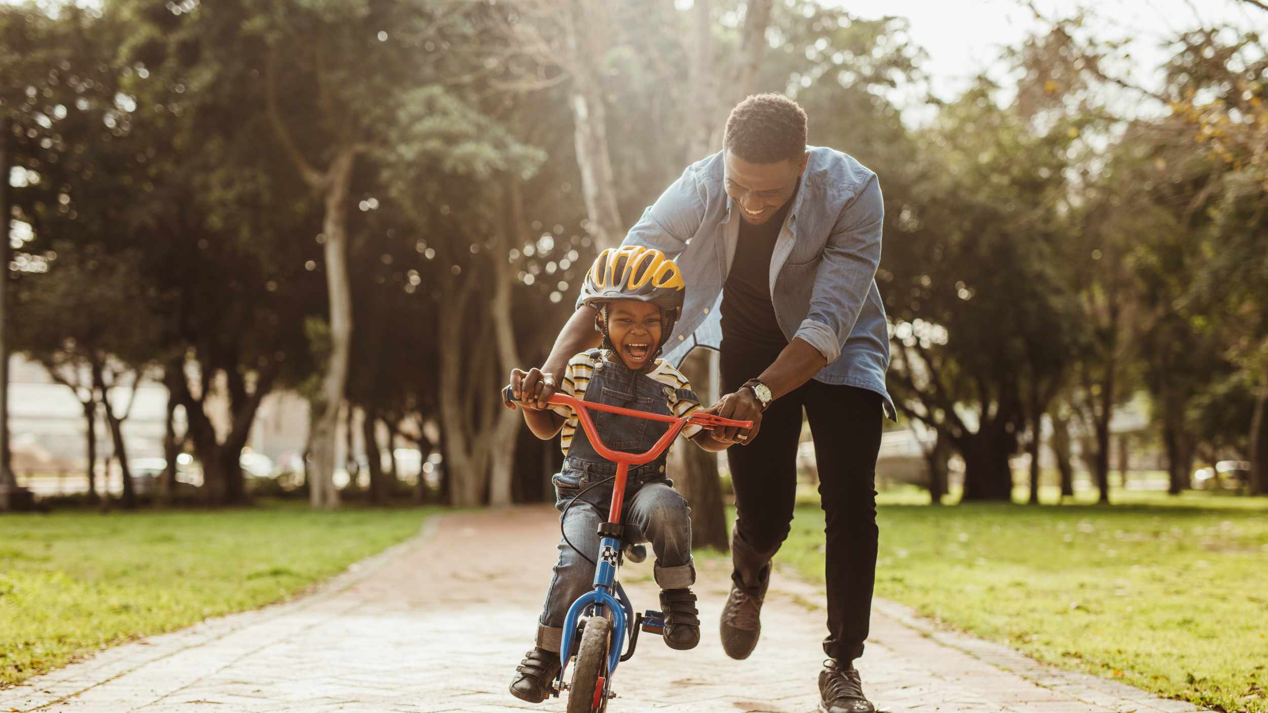 Boy learning to ride a bicycle with his father in park. Father teaching his son cycling at park.