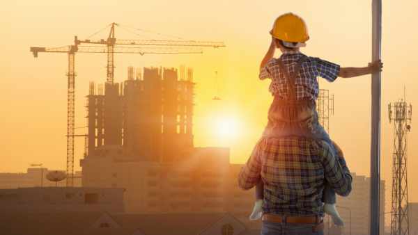 Asian boy on father’s shoulders with background of new high buildings and silhouette construction cranes of evening sunset, father and son concept