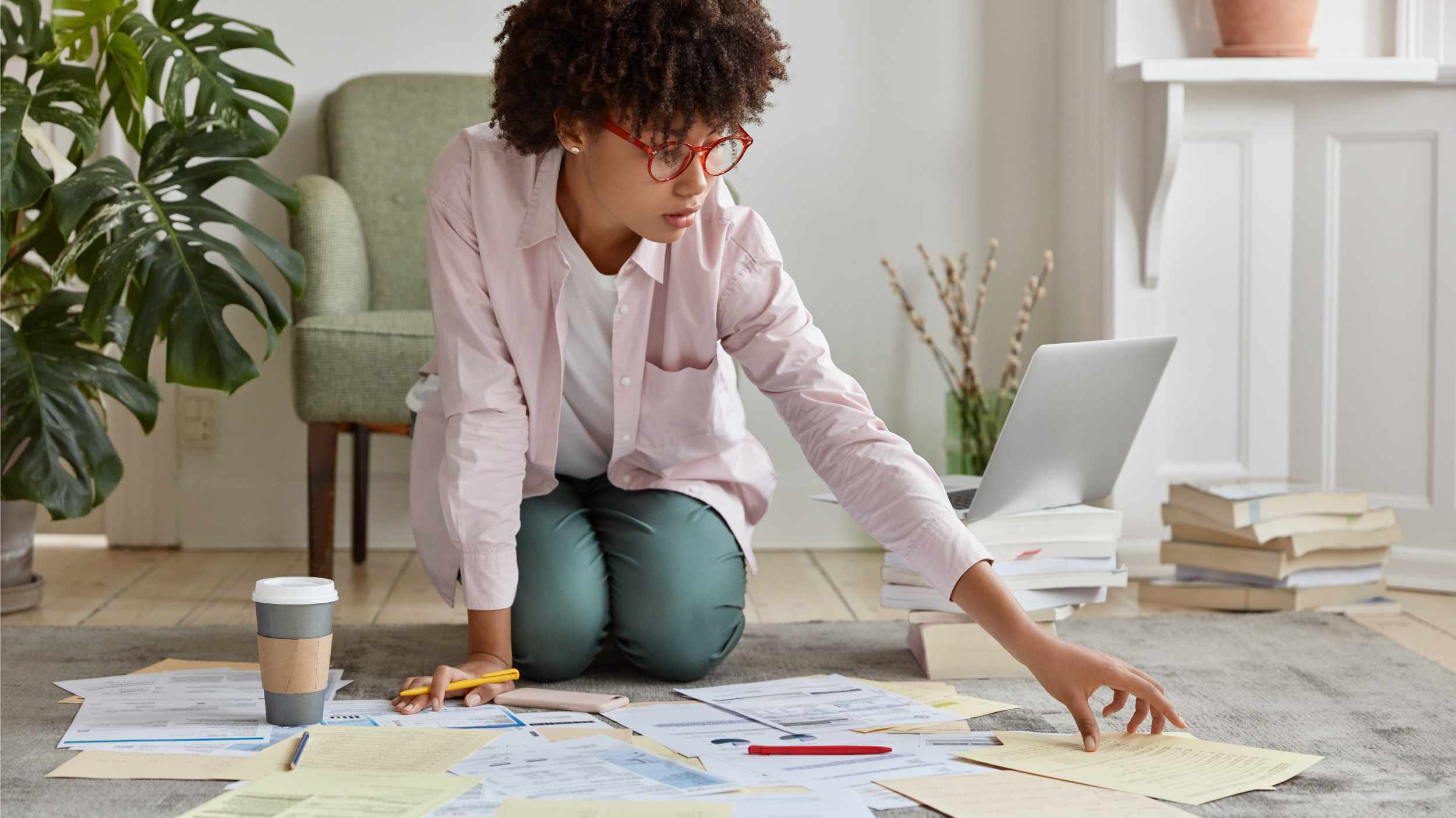 Black marketing director faces financial disclosure, studies economic forces, surrounded with much papers, dressed in casual shirt, spectacles, poses on floor of cozy apartment. Business education