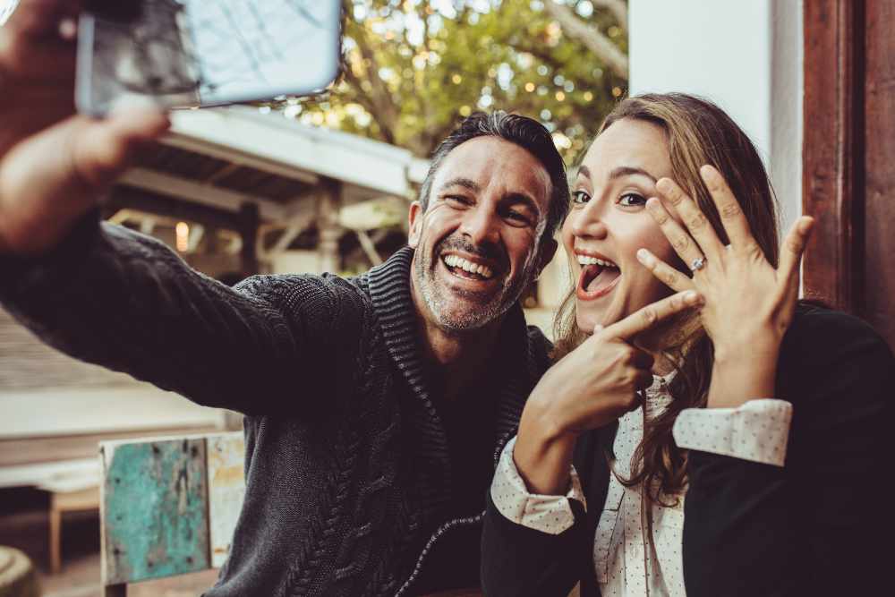 Affectionate couple announcing their engagement with selfies while sitting at cafe. Happy couple taking a selfie and showing off their wedding ring at coffee shop.