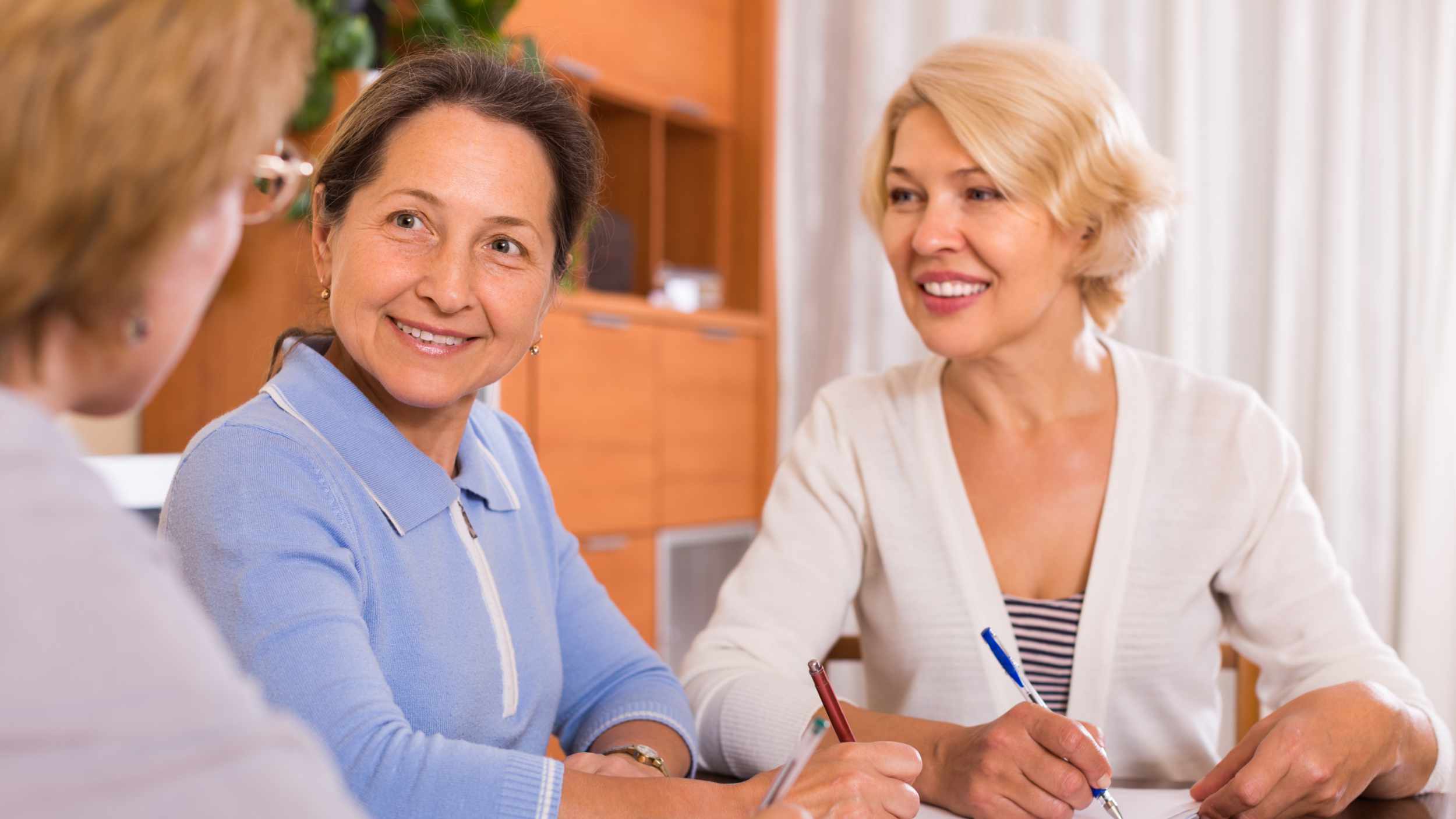 Positive senior ladies signing documents at notary. Focus on brunette