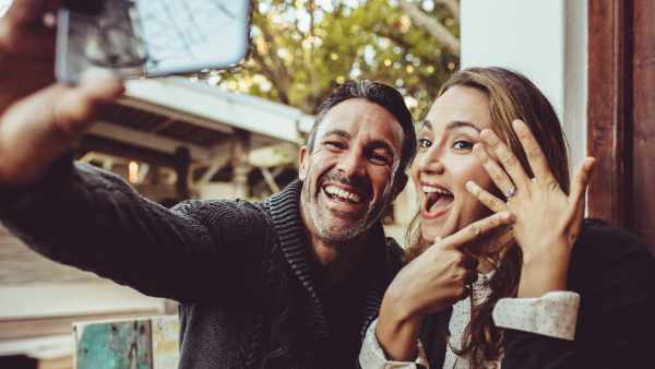 Affectionate couple announcing their engagement with selfies while sitting at cafe. Happy couple taking a selfie and showing off their wedding ring at coffee shop.