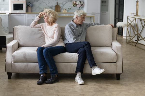 Angry frustrated tired senior couple sitting separately on home couch in silence, looking away, ignoring, thinking over relationship problems, divorce, breakup, marriage crisis